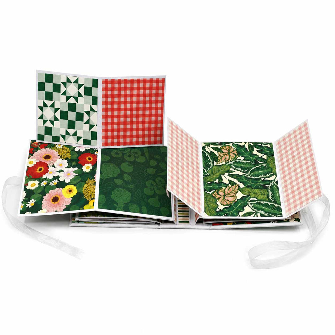 A fabric scrapbook album shown open, displaying multiple patterned and printed interior pages with ribbon ties on a white background.