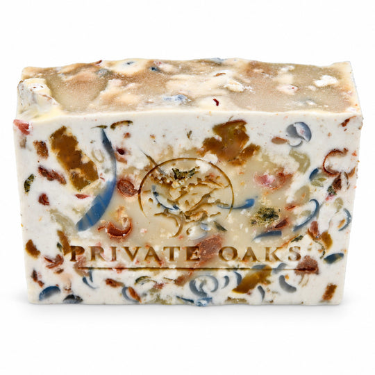 A rectangular bar of handmade soap with a cream-colored base, decorated with embedded brown, blue, and red botanical pieces. The bar features an embossed circular logo and the text 'PRIVATE OAKS' printed on the front, set against a plain white background.
