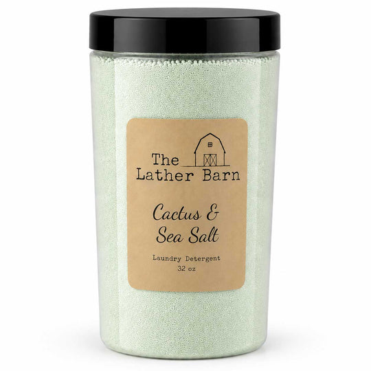 A 32 oz jar of The Lather Barn Cactus & Sea Salt laundry detergent. The product consists of pale green sea salt granules inside a clear plastic jar with a black lid and a tan paper label.