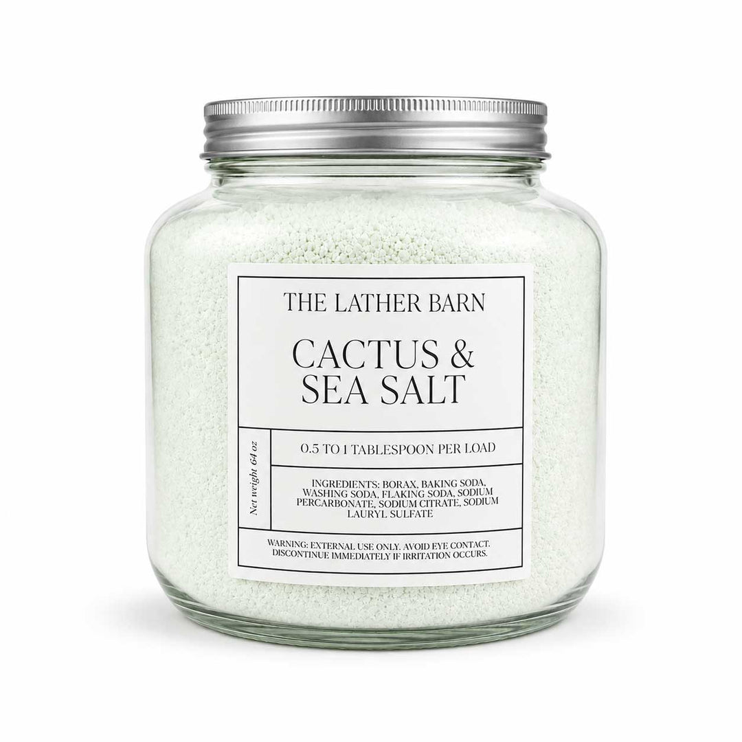 A clear glass jar filled with pale sea salt crystals and topped with a silver metal lid, labeled 'THE LATHER BARN CACTUS & SEA SALT' on a white background.