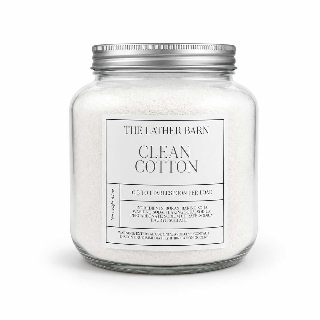 A glass jar candle filled with white cotton bath salts, featuring a silver metal lid and a white label that reads 'THE LATHER BARN CLEAN COTTON'.