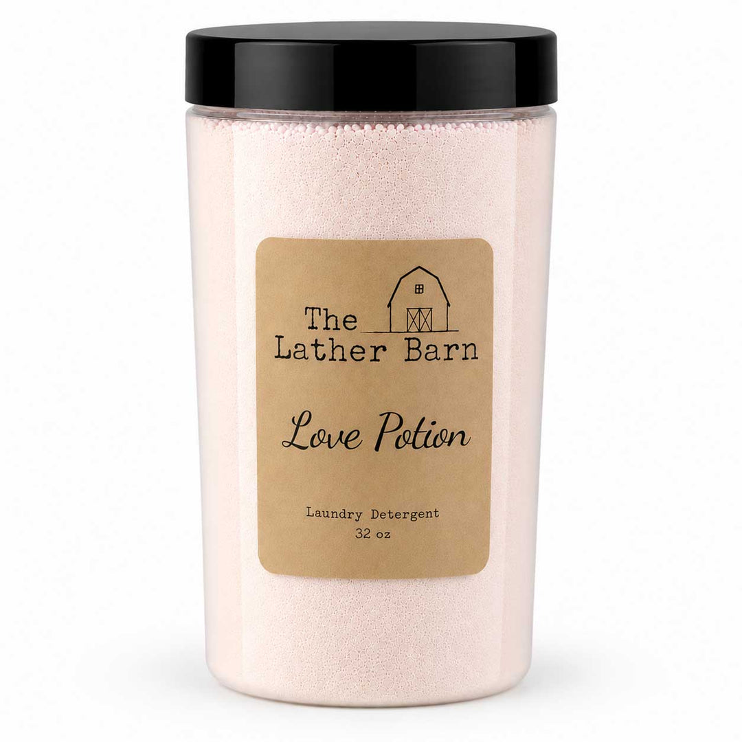 A clear plastic jar of laundry detergent with a black lid and a tan label reading 'The Lather Barn Love Potion Laundry Detergent 32 oz' on a white background.