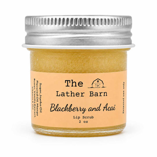 A 2 oz glass jar of The Lather Barn Blackberry and Acai Lip Scrub, filled with a golden-yellow scrub and topped with a silver metal screw cap, set against a plain white background.