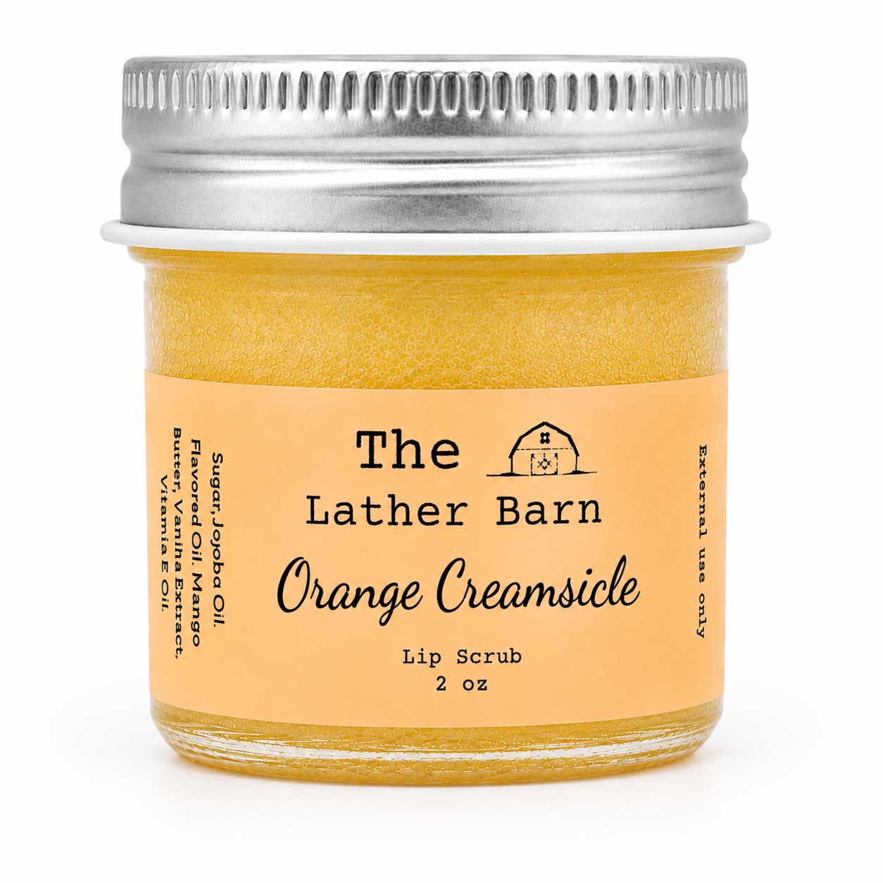 A 2 oz glass jar of The Lather Barn Orange Creamsicle Lip Scrub, filled with a golden-yellow scrub and featuring a peach-colored label with a silver metal screw cap, set against a plain white background.