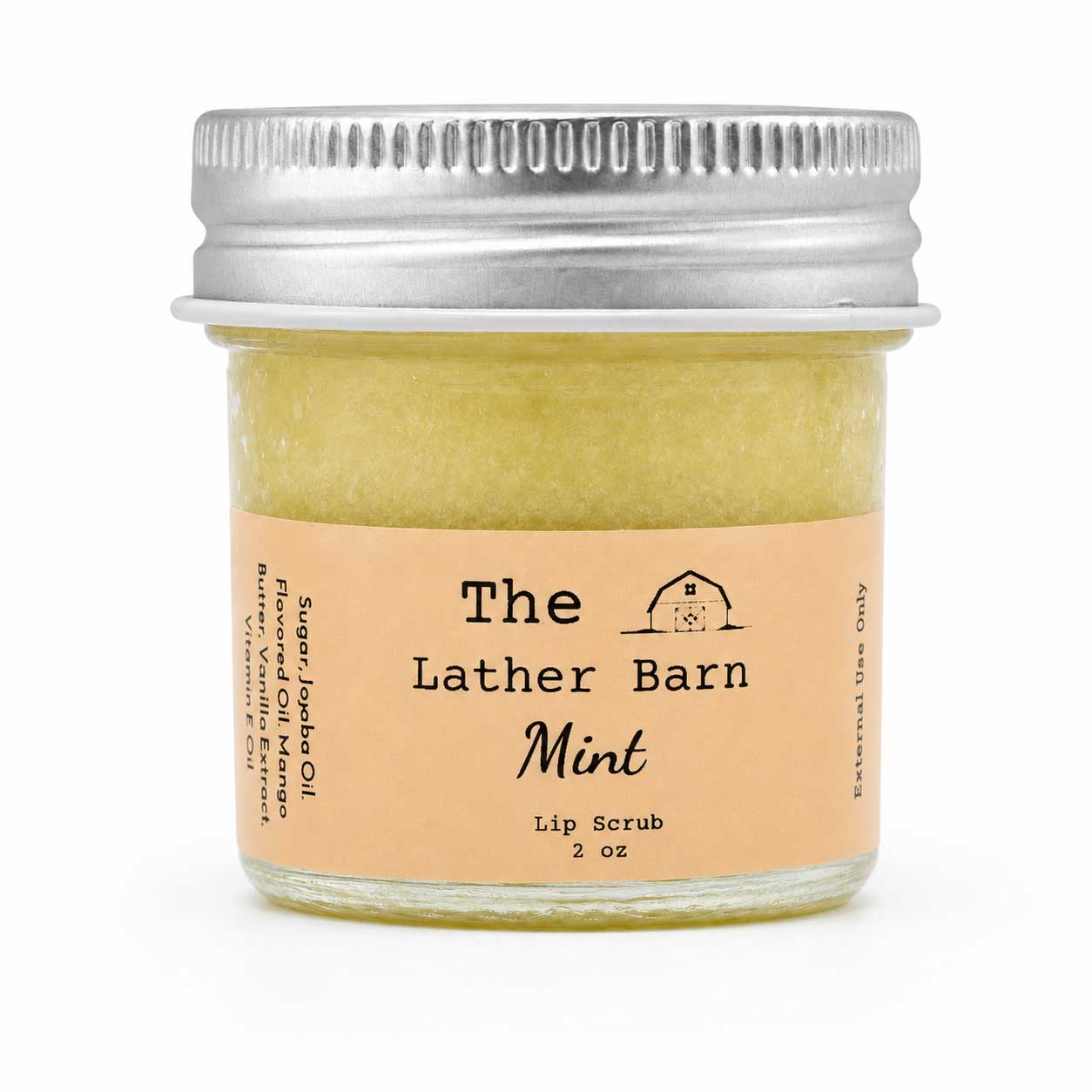 A small glass jar of mint lip scrub with a silver metal lid and a peach-colored label reading 'The Lather Barn Mint Lip Scrub 2 oz'.