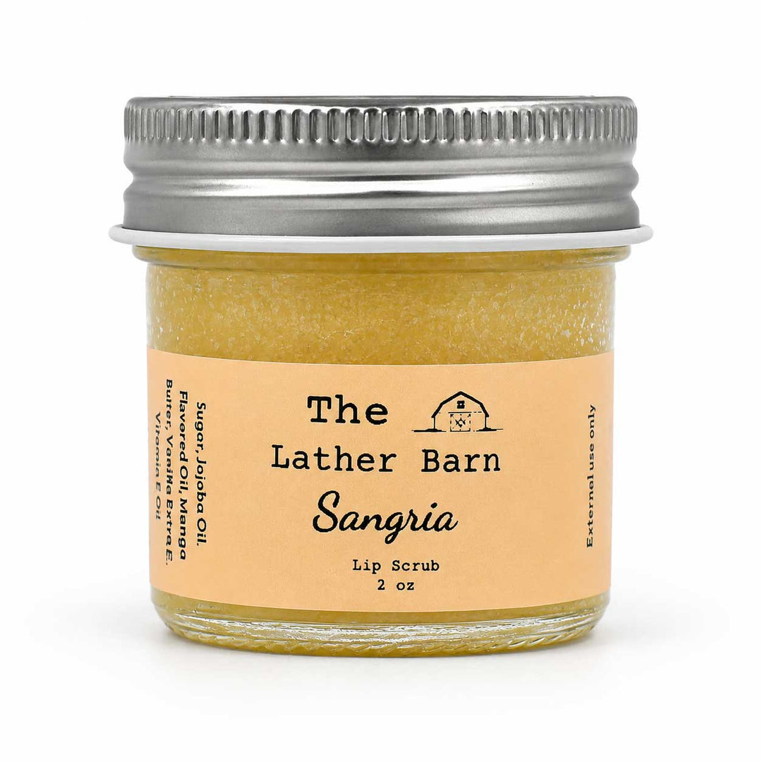 A 2 oz glass jar of 'The Lather Barn' Sangria Lip Scrub, filled with a yellowish-amber scrub and featuring a light peach label with a silver metal screw lid, set against a plain white background.