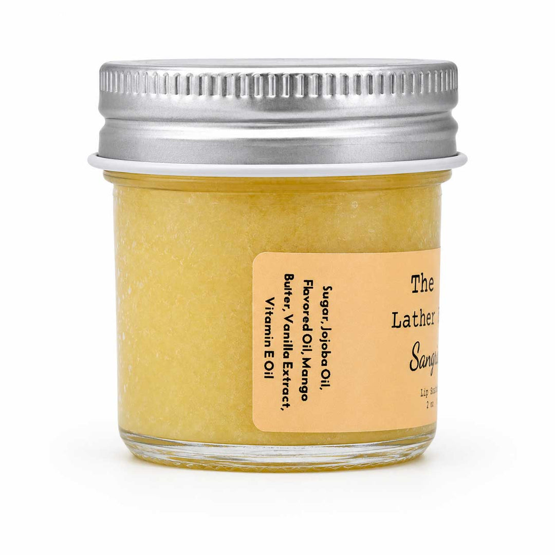 A small clear glass jar filled with pale yellow scrub or balm, sealed with a silver metal screw lid and labeled 'The Lather Soap' on a white background.
