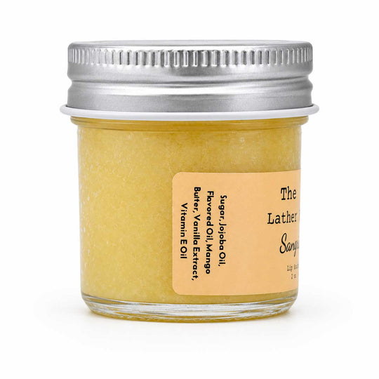 A small clear glass jar filled with pale yellow scrub or balm, sealed with a silver metal screw lid and labeled 'The Lather Soap' on a white background.