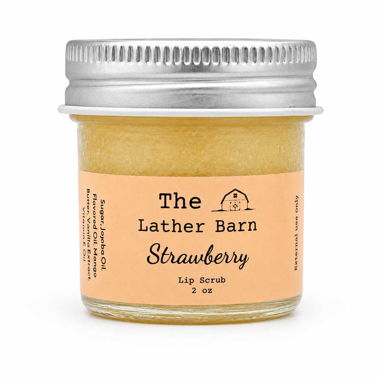 A small glass jar of strawberry lip scrub by The Lather Barn, filled with a pale yellowish-amber scrub and topped with a silver metal screw lid. The front label is peach-colored with black text.