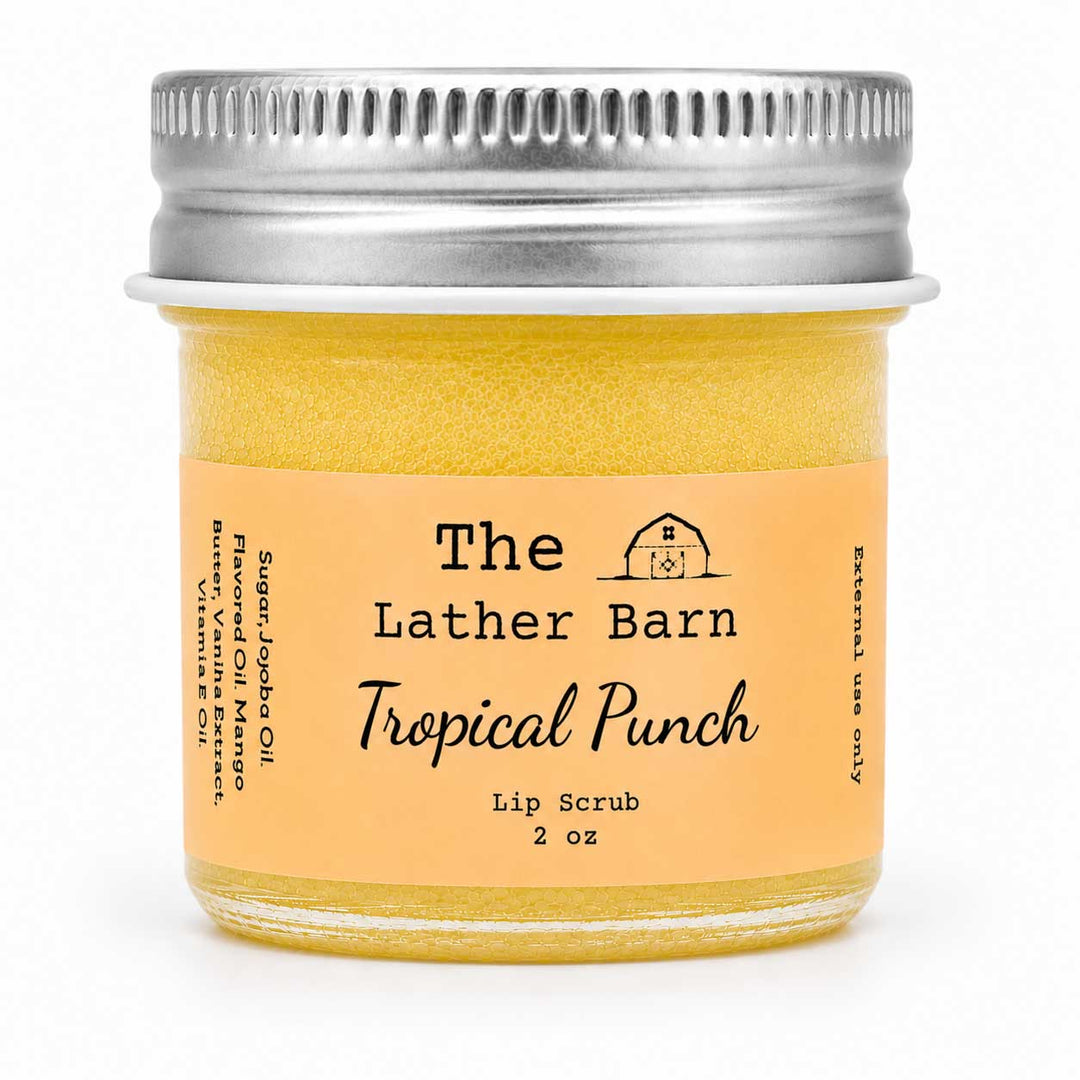 A 2 oz glass jar of The Lather Barn Tropical Punch Lip Scrub, filled with a yellow-orange scrub and featuring a peach-colored label with a silver metal screw cap, set against a plain white background.