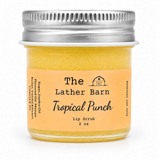A 2 oz glass jar of The Lather Barn Tropical Punch Lip Scrub, filled with a yellow-orange scrub and featuring a peach-colored label with a silver metal screw cap, set against a plain white background.