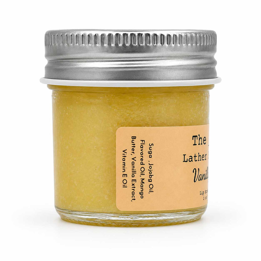A small glass jar of yellow lather soap with a silver metal screw lid and a tan label, photographed on a clean white background.
