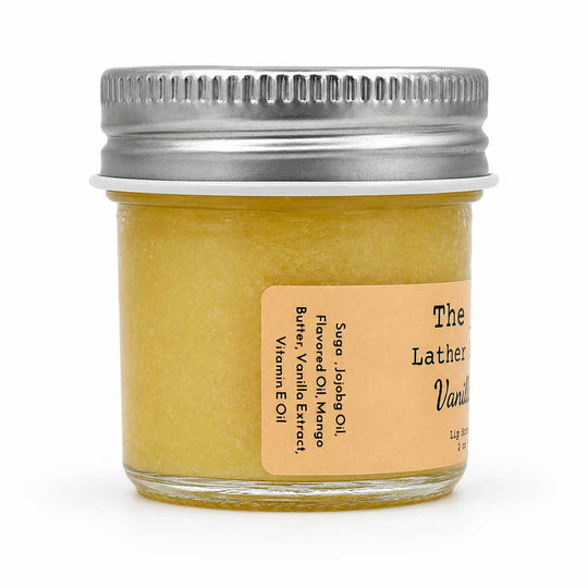 A small glass jar of yellow lather soap with a silver metal screw lid and a tan label, photographed on a clean white background.