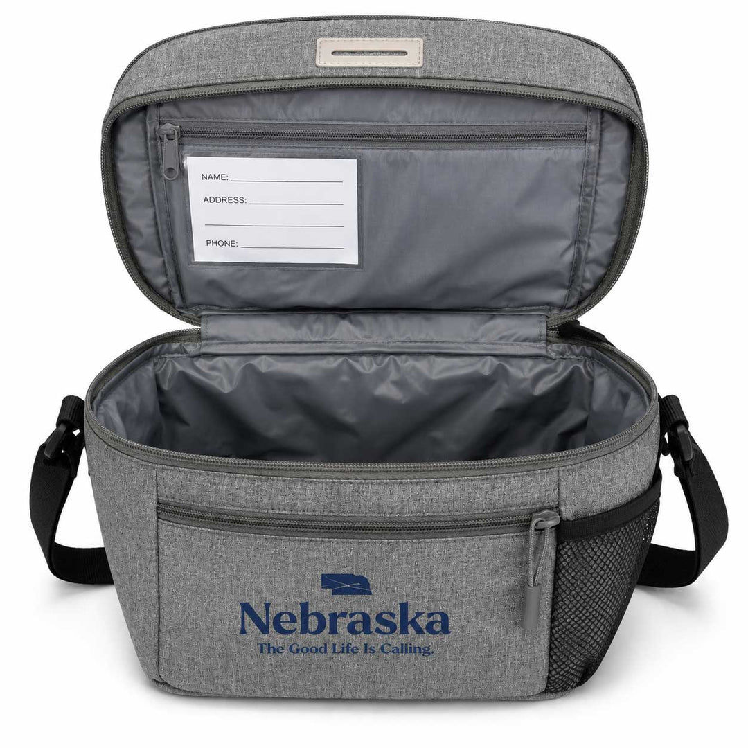 Gray heather insulated cooler bag shown open, with a front zip pocket printed with the Nebraska logo, black shoulder straps, and a gray interior including a name/address/phone label on the inside lid.
