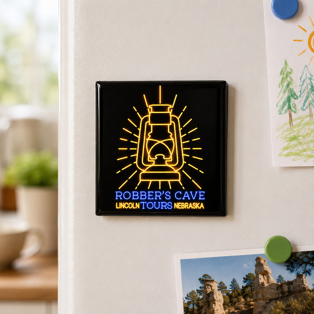 A square black refrigerator magnet featuring a yellow line-art lantern and the text 'ROBBER'S CAVE LINCOLN TOURS NEBRASKA' in blue and yellow, shown attached to a white refrigerator door in a home setting.