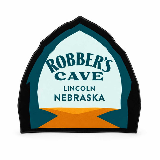 A die-cut magnet featuring the logo for 'Robber's Cave Lincoln Nebraska' in a stylized arch shape with a black border, teal and light blue center, and orange accents at the bottom, shown on a plain white background.