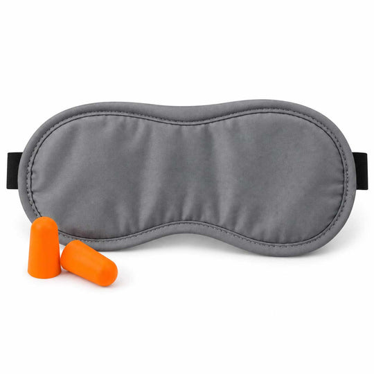 A gray padded sleep mask with black elastic straps, shown on a white background with two bright orange earplugs in front.