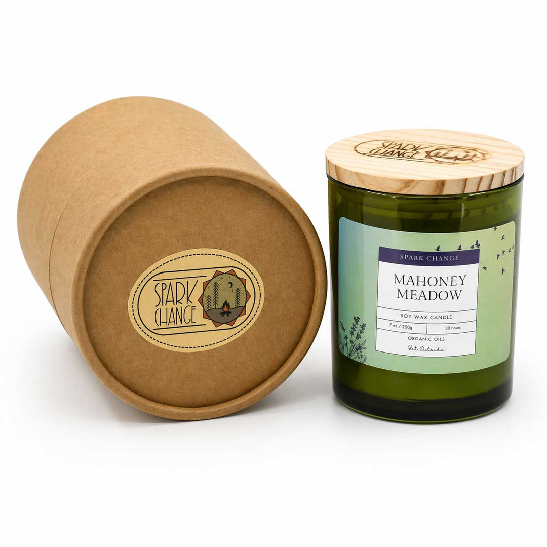 Candle labeled 'Mahoney Meadow' with a wooden lid next to its brown cardboard packaging on a white background.