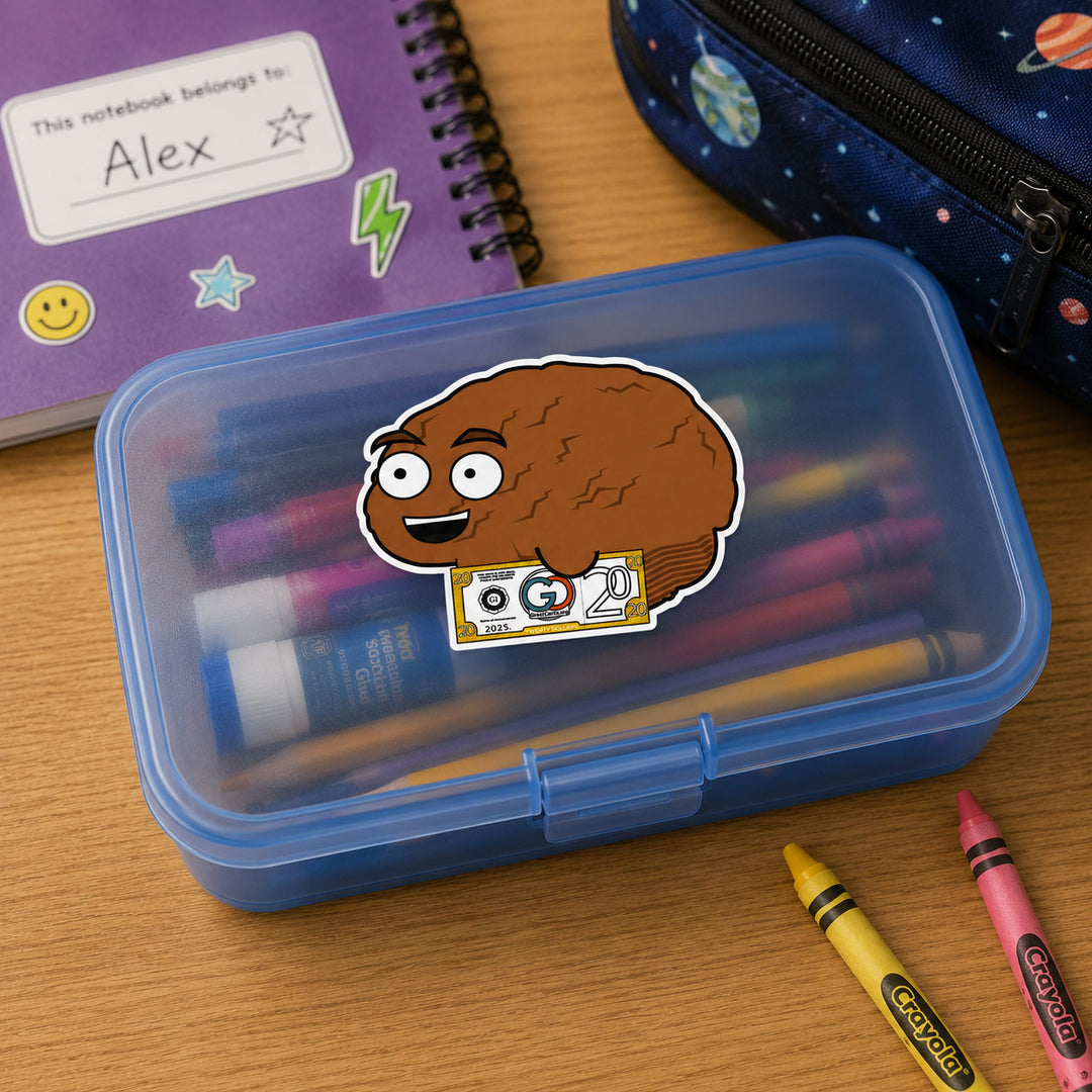 A blue plastic pencil case with a clear lid, featuring a cartoon sticker of a brown brain character holding a cassette tape. The case is open and filled with colorful pens, placed on a wooden desk alongside other school supplies including a purple notebook, a starry blue pencil case, and crayons.