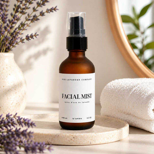 Facial mist bottle labeled 'Our Lavender Company' on a wooden surface with lavender flowers and a towel.