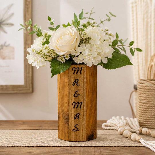 Wooden vase with engraved initials 'M R & MRS' holding a floral arrangement on a table.