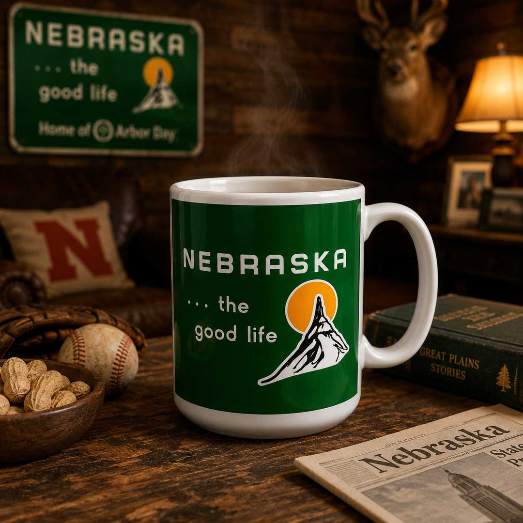 A white ceramic mug with a green Nebraska-themed wraparound print reading '.