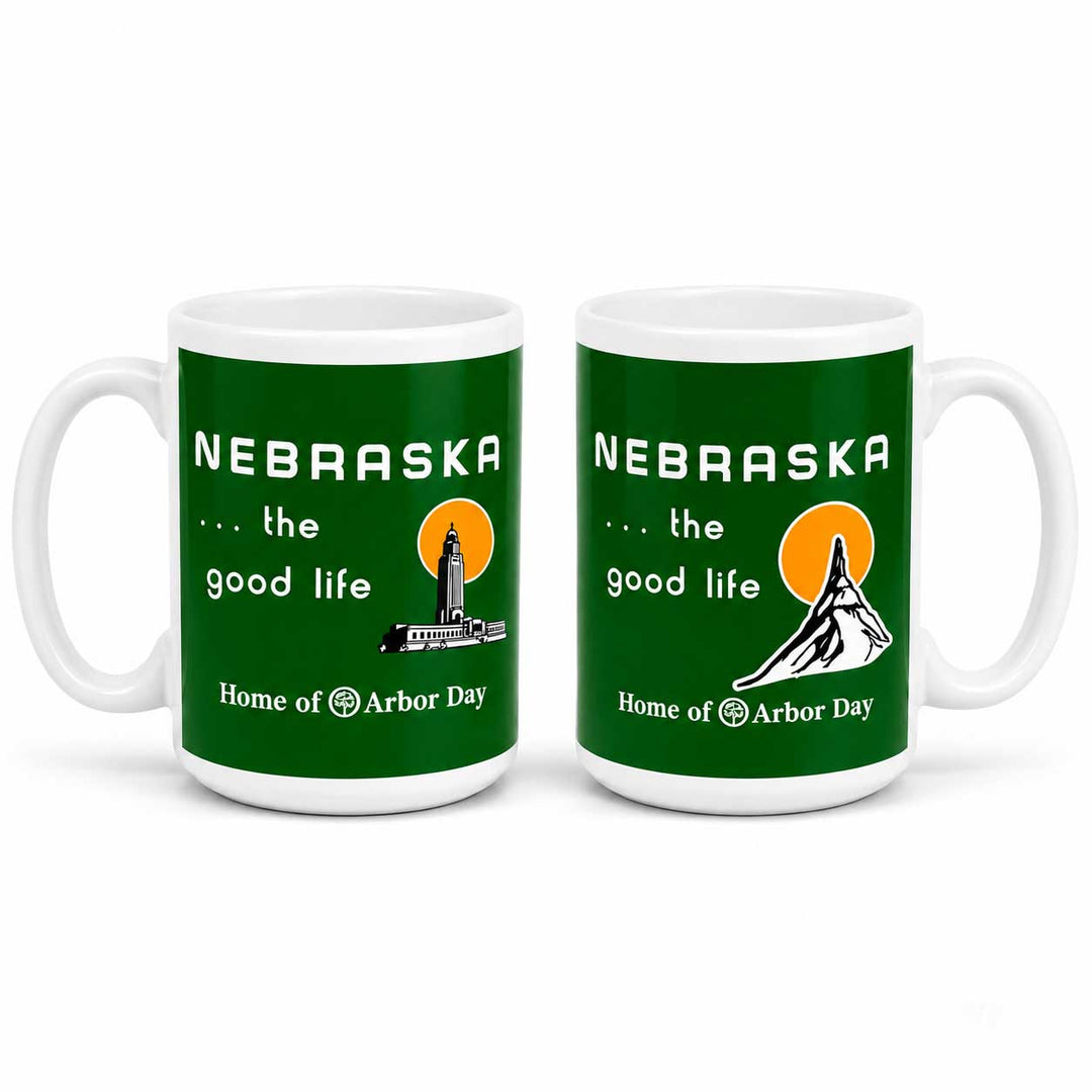 Two white ceramic mugs with a green Nebraska graphic design, shown side by side on a white background. The design features the text 'NEBRASKA .