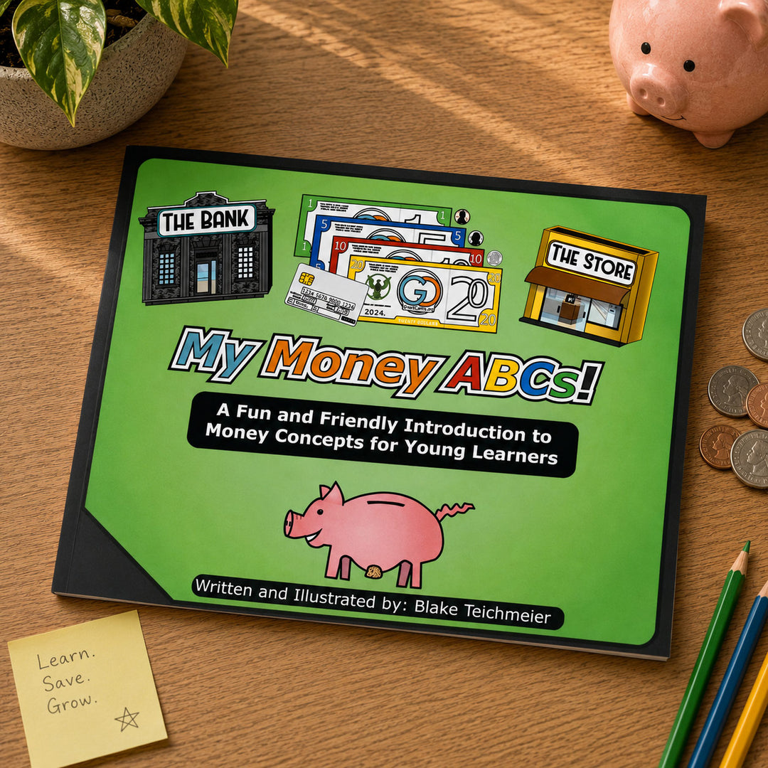 A children's book titled "My Money ABCs!" lies on a wooden desk, surrounded by a piggy bank, plant leaves, coins, colored pencils, and a sticky note. The cover is bright green with cartoon illustrations of a bank, store, money, and a pig.