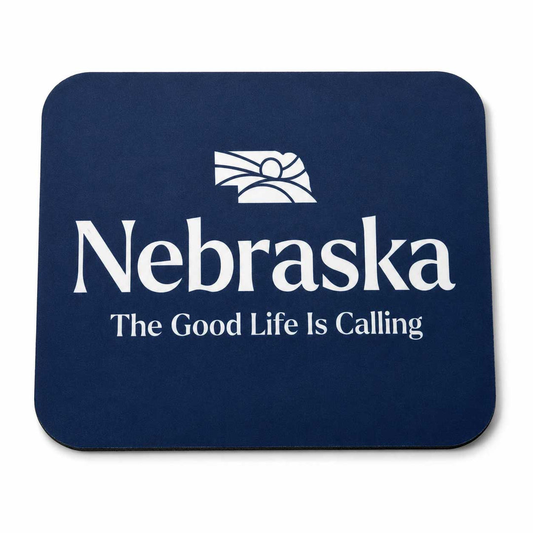 A dark navy blue rectangular mouse pad with rounded corners, featuring a white printed Nebraska state outline and the words 'Nebraska' and 'The Good Life Is Calling' on a white background.