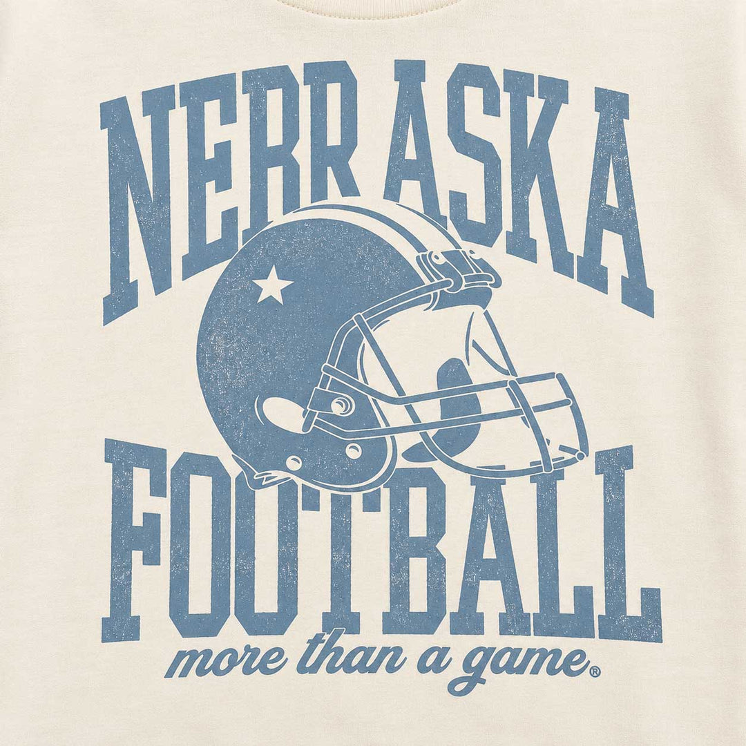 Close-up of a cream-colored t-shirt featuring a distressed blue graphic that reads 'NEBRASKA FOOTBALL more than a game' with a football helmet illustration in the center.