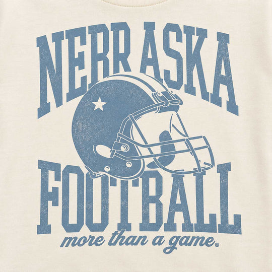 Close-up of a cream-colored t-shirt featuring a distressed blue graphic that reads 'NEBRASKA FOOTBALL more than a game' with a football helmet illustration in the center.