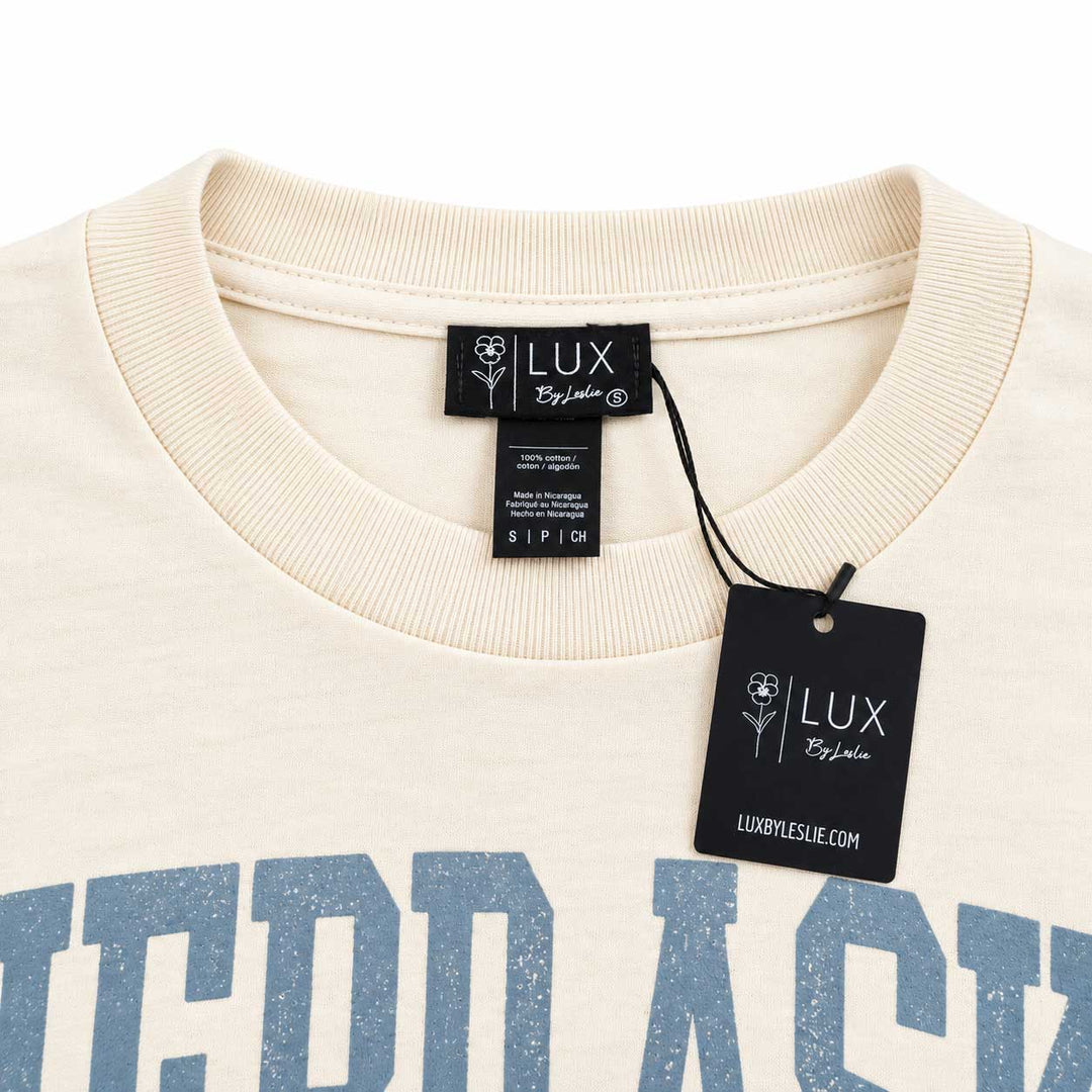 Close-up of a cream-colored ribbed crewneck sweatshirt with a blue graphic print, featuring a black 'LUX Bespoke' brand tag and hangtag.