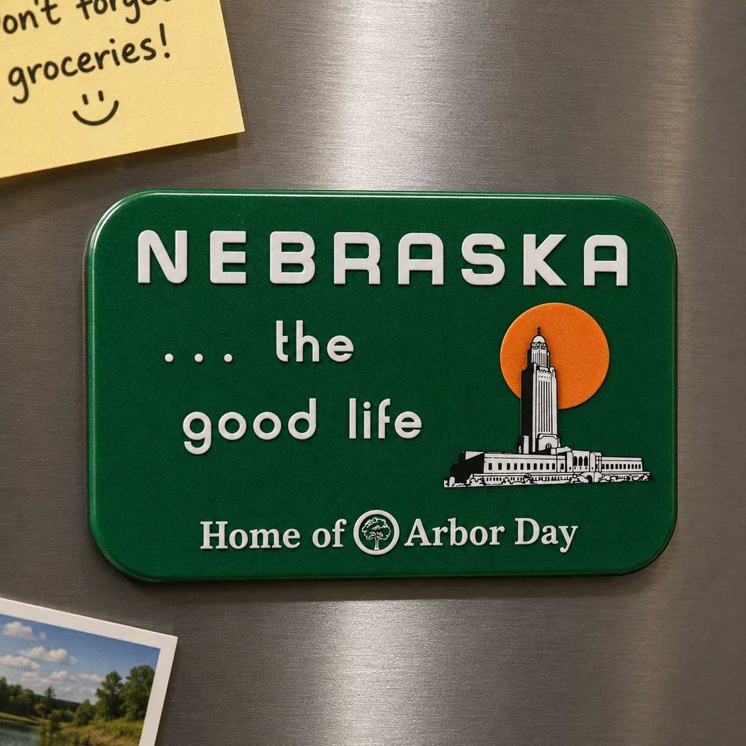A green rectangular refrigerator magnet with rounded corners featuring the text 'NEBRASKA .