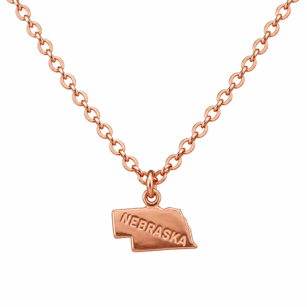 A rose gold necklace with a small engraved 'NEBRASKA' pendant shaped like the state of Nebraska, shown on a plain white background.