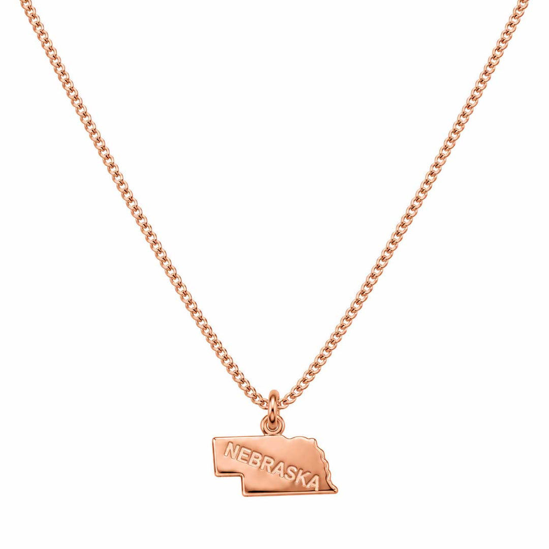 A rose gold necklace featuring a small pendant shaped like the state of Nebraska, with the word 'NEBRASKA' engraved on it, displayed against a solid white background.