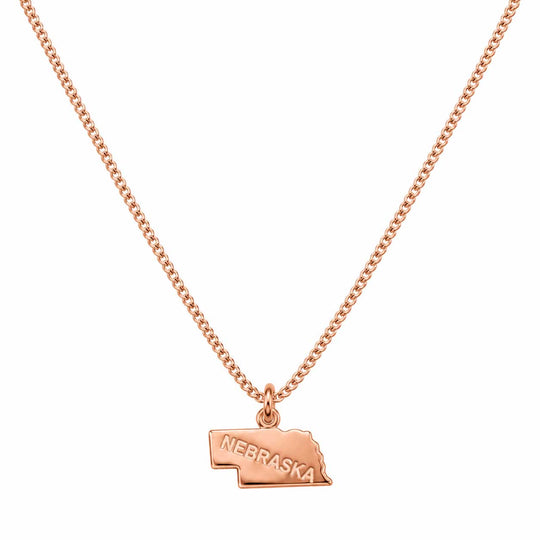 A rose gold necklace featuring a small pendant shaped like the state of Nebraska, with the word 'NEBRASKA' engraved on it, displayed against a solid white background.