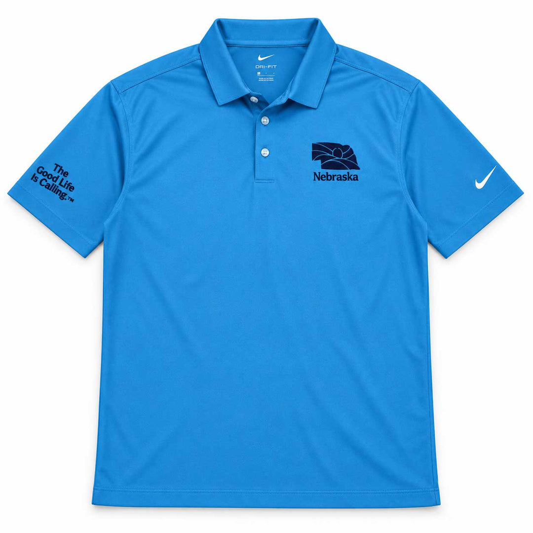 A bright blue Nike polo shirt with Nebraska branding, featuring a dark navy Nebraska Cornhuskers logo on the left chest and 'The Good Life is Hailing' text on the right sleeve, shown against a plain white background.
