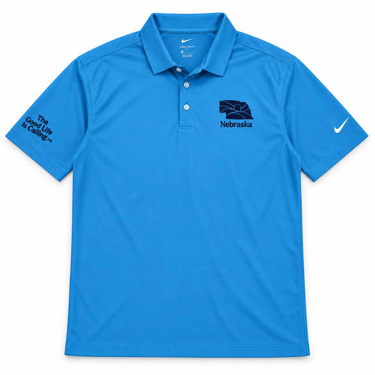 A bright blue Nike polo shirt with Nebraska branding, featuring a dark navy Nebraska Cornhuskers logo on the left chest and 'The Good Life is Hailing' text on the right sleeve, shown against a plain white background.