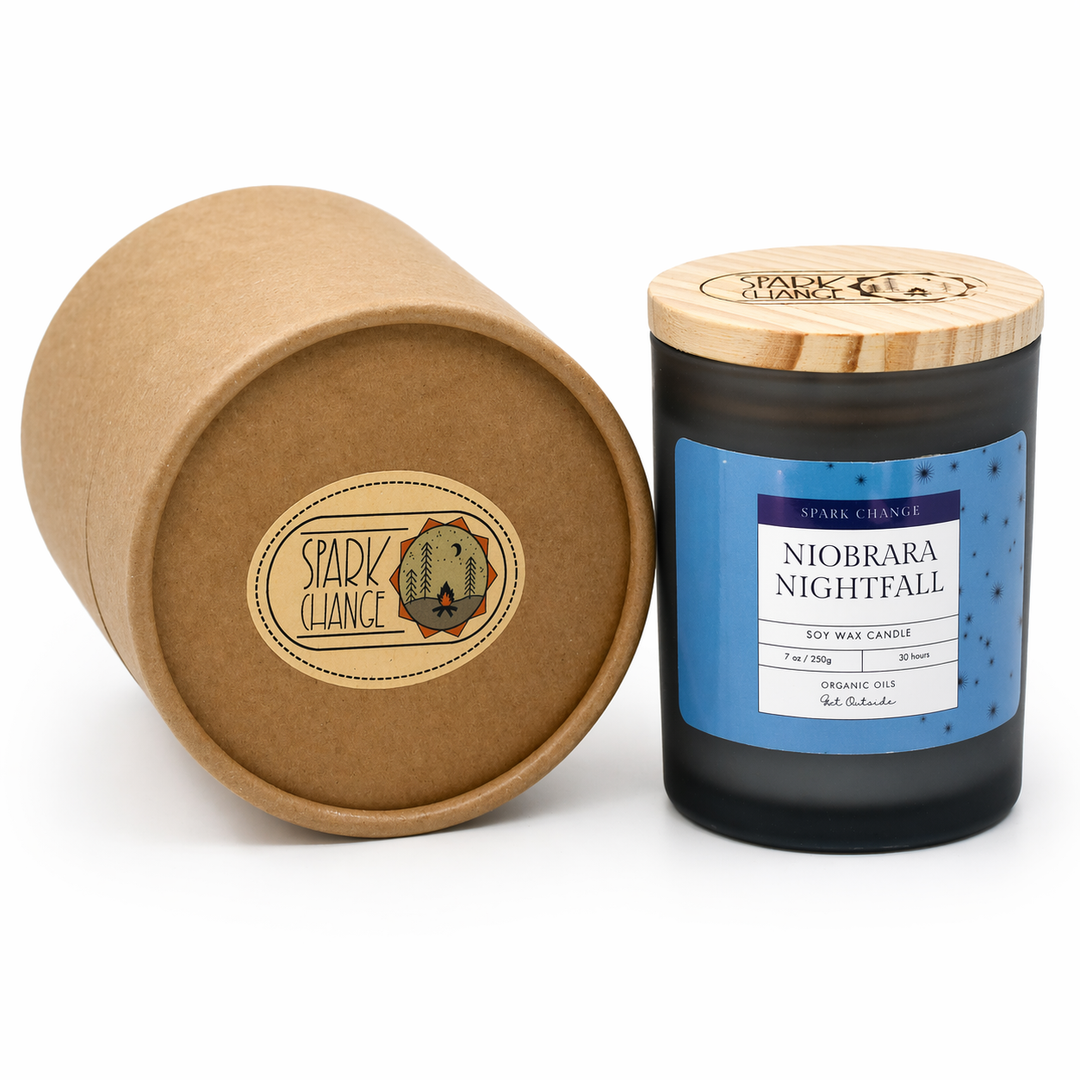Candle with a blue label and wooden lid next to an open cardboard tube with a brand logo.