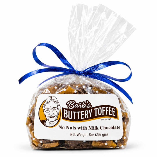 A 8 oz bag of Barb's Buttery Toffee, no nuts with milk chocolate, wrapped in clear cellophane, tied with a blue ribbon, and featuring a white label with the brand logo.