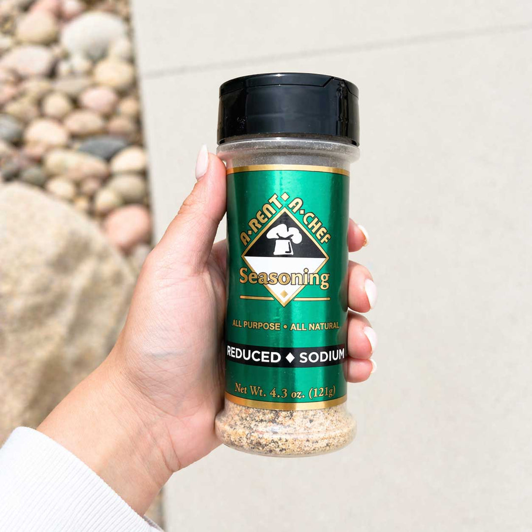 Hand holding a jar of reduced sodium seasoning with a natural stone background