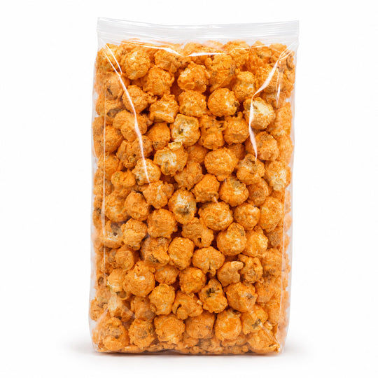 A clear plastic bag filled with orange-coated popcorn pieces, photographed upright on a clean white background.