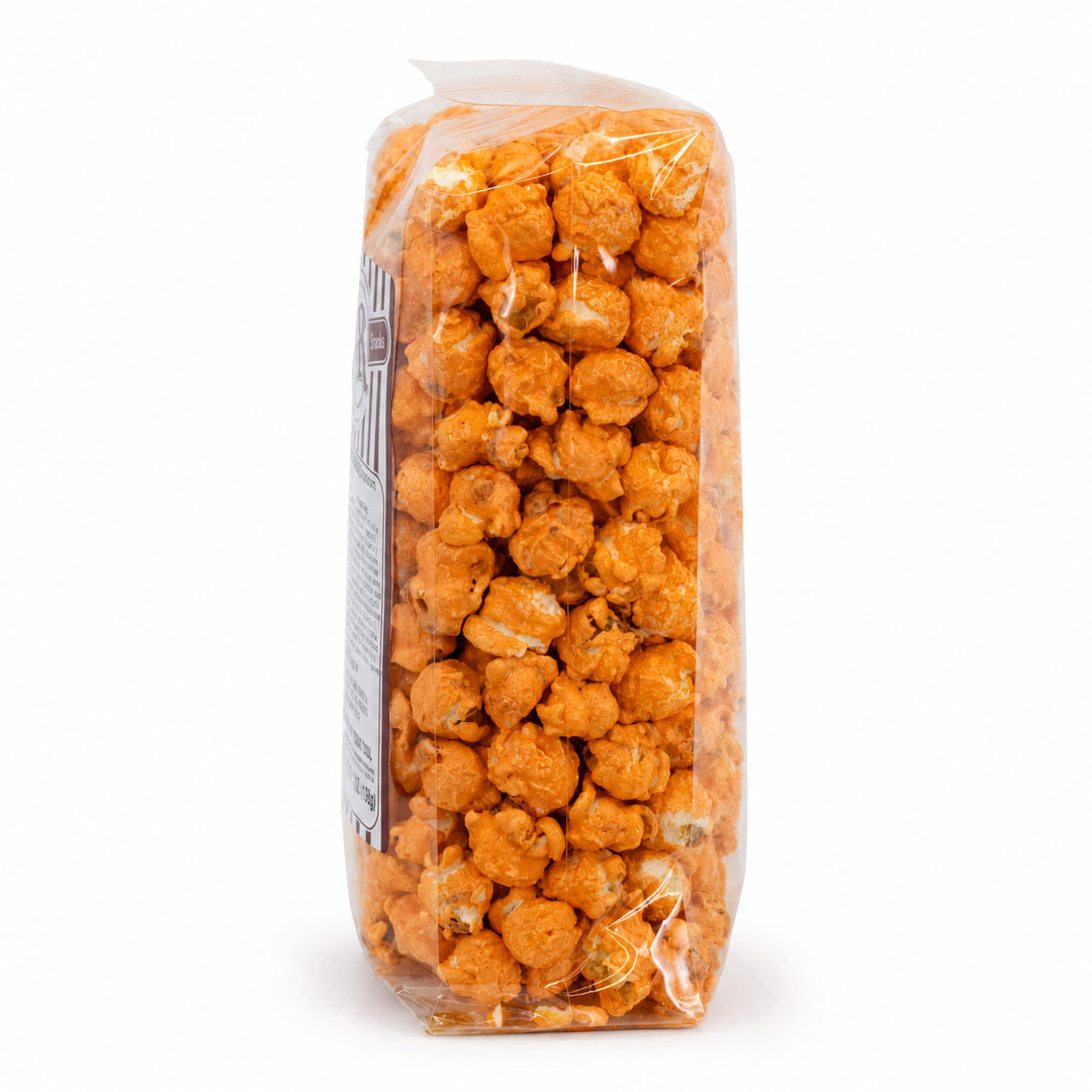 A clear plastic bag filled with orange-coated popcorn pieces, photographed upright on a plain white background.