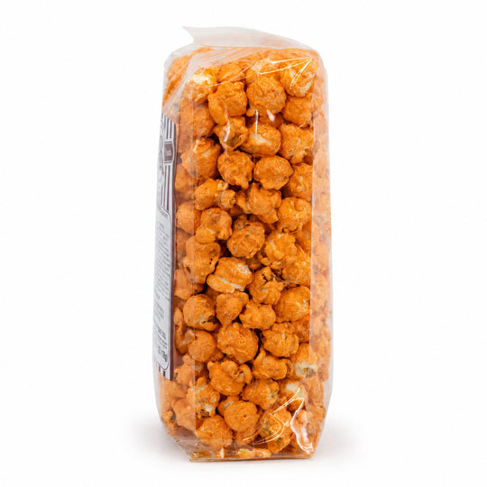 A clear plastic bag filled with orange-coated popcorn pieces, photographed upright on a plain white background.