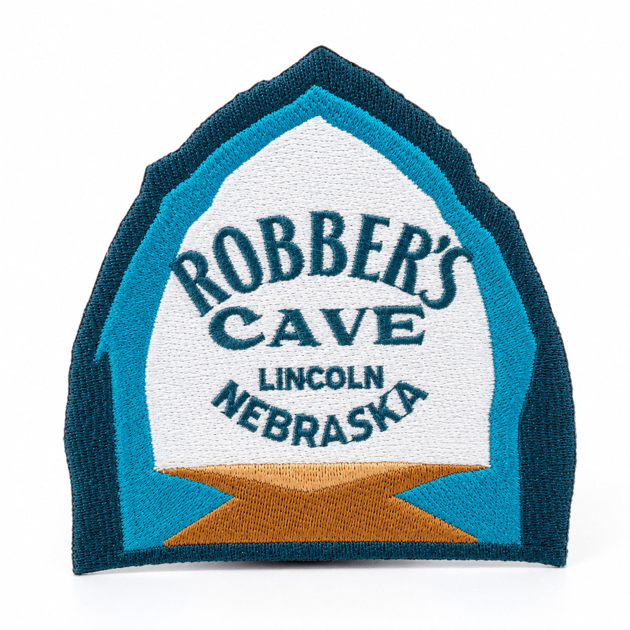 An embroidered patch shaped like a tombstone, featuring the text 'ROBBER'S CAVE LINCOLN NEBRASKA' in dark blue embroidery on a white background, surrounded by a teal border and a gold star at the bottom, set against a plain white background.