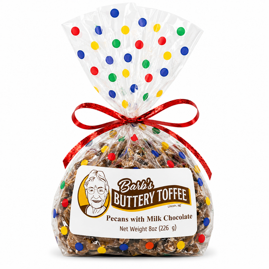 A 8 oz bag of Barb's Buttery Toffee Pecans with Milk Chocolate, wrapped in clear cellophane with a red ribbon and a polka-dot decorated top, on a white background.