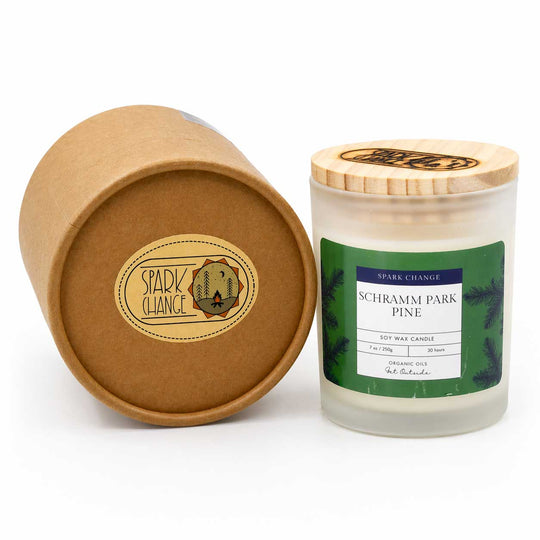 Candle with wooden lid and Schramm Park Pine label, next to a cardboard tube with 'Spark Change' branding.
