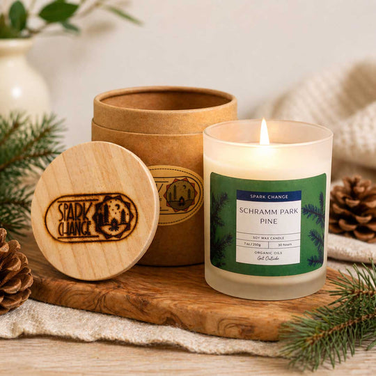 Candle with wooden container and label on a wooden surface with pine branches.