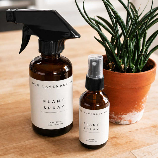 Two bottles of plant spray with labels next to a potted plant on a wooden surface.