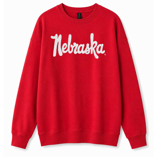 A bright red crewneck sweatshirt featuring the word 'Nebraska' printed across the chest in a white cursive script, displayed against a clean white background.